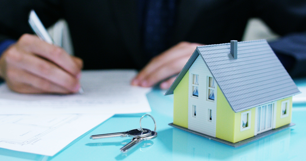 the hands of an insurer or real estate agent showing a house with floor plan and documents